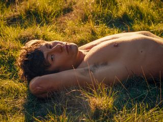 barry keoghan as oliver quick, lying shirtless in a grassy field, in the 2023 movie saltburn
