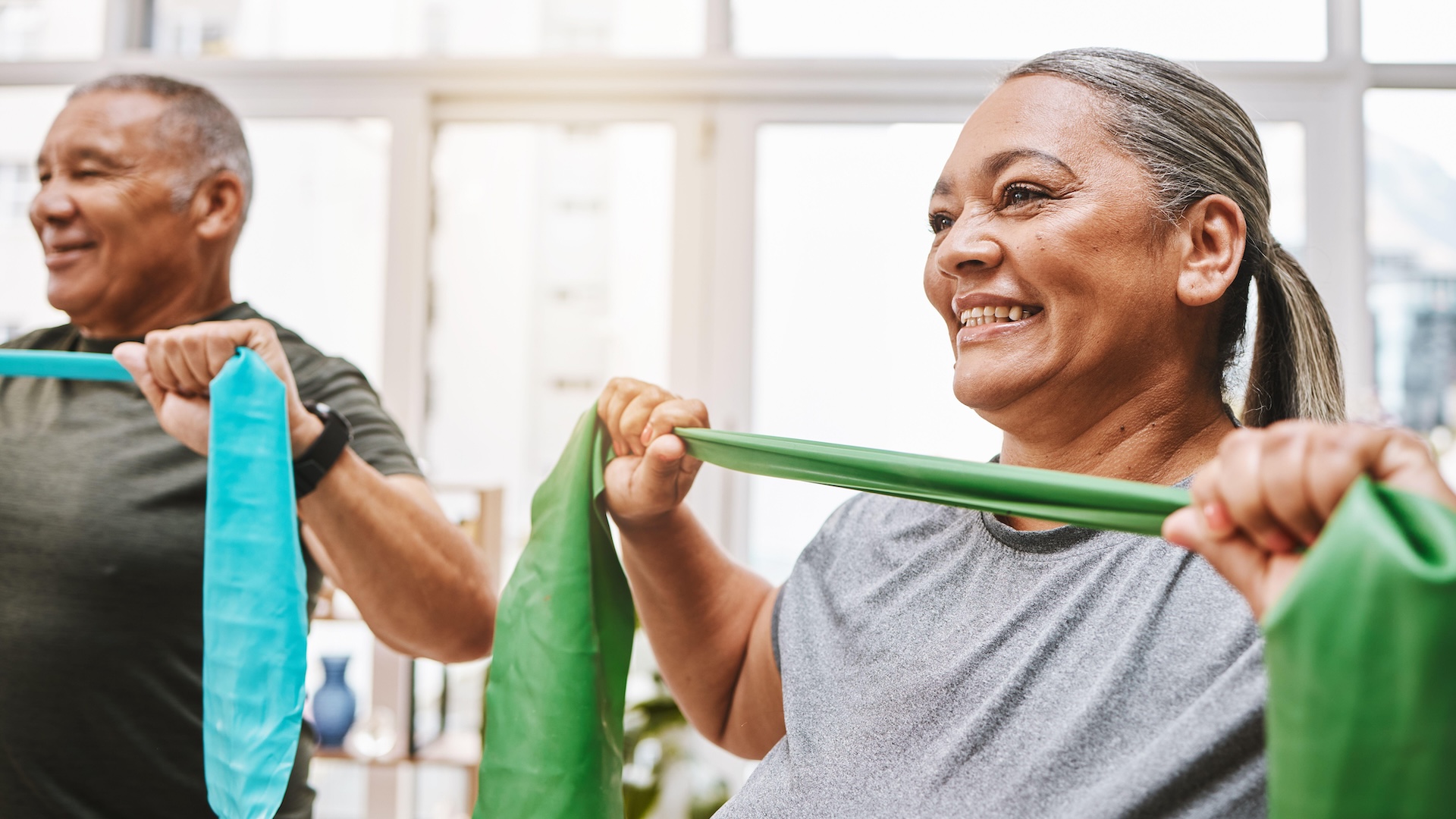 An older woman and man stretch resistance bands.