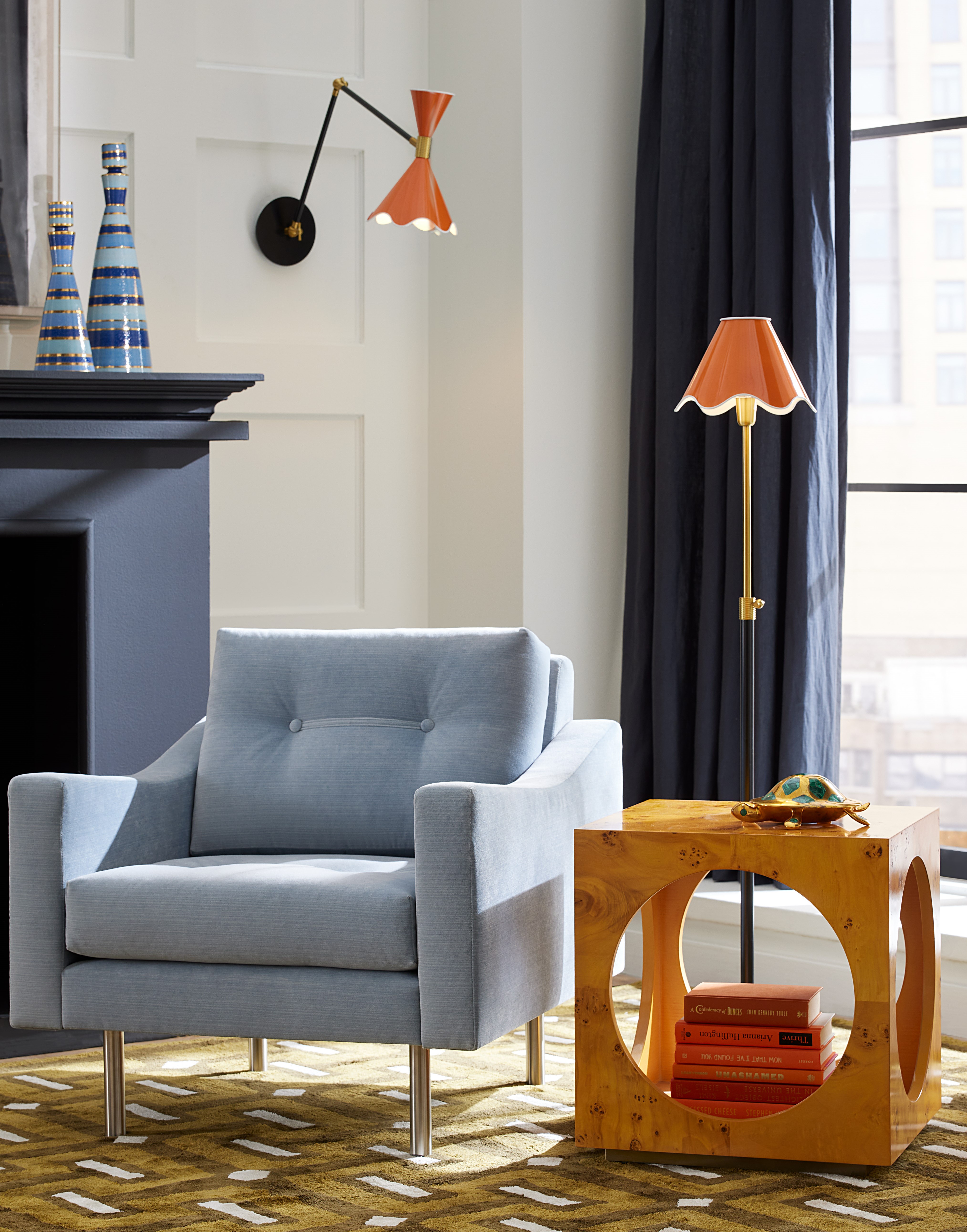 A Jonathan Adler scalloped floor lamp pixtured in a mid-century-inspired living room with a geometric green rug and blue accent chair