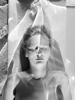 Black and white photo of a woman lying on a towel with water reflections on her