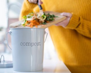 a woman throwing food scraps into a white compost bin/caddy