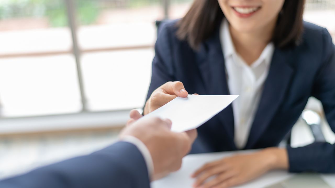 A woman receives an envelope containing her bonus in an office.