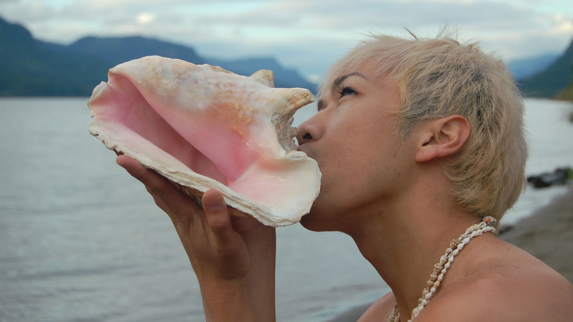 an image of a man blowing into a conch shell on a beach