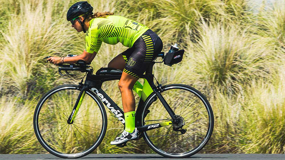 person riding a tt bike in full cycling gear on the road in front if some green vegetation