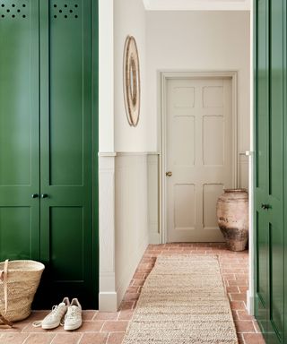 Hallway with green paintwork on cabinets, brick flooring and sisal runner towards door.