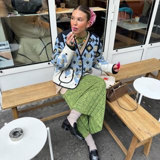 a woman wears a colorful printed jacket with a green skirt