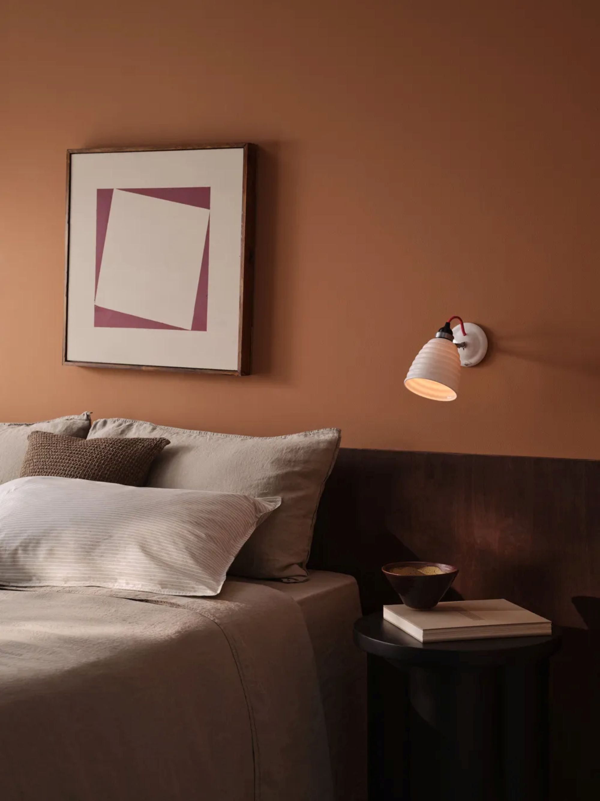 bedroom with burnt orange walls, a light taupe bedspread, wall art, and a white wall sconce