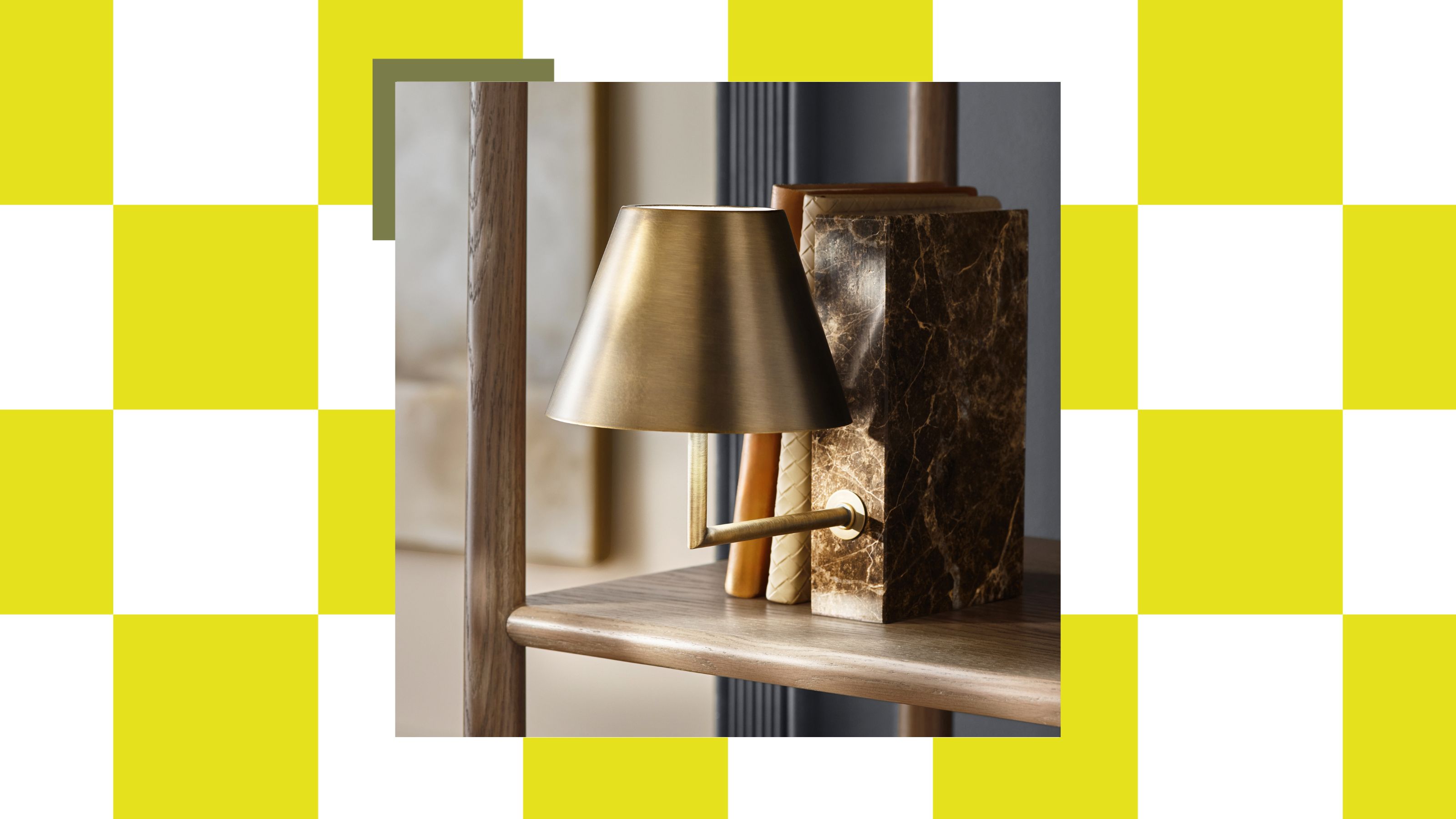 A marble book-shaped-base rechargeable lamp with a brass shade attached from the front on a bookshelf with a couple of books leaning against it