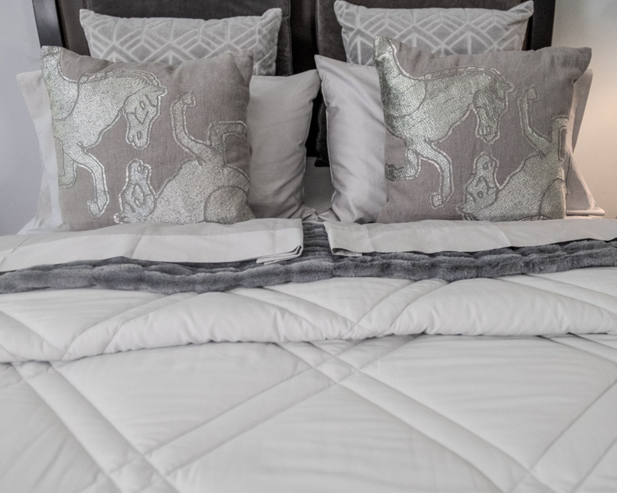 The Dreamwings bed sheets shown on a neatly made bed with a white comforter and silvery cushions decorated with horses.