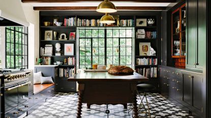 A kitchen with black and white floor tiles, black bookcases and a spanish style kitchen table with spindle legs 