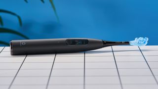 a black electric toothbrush with a small touchscreen and a blue toothbrush head and a square charging stand