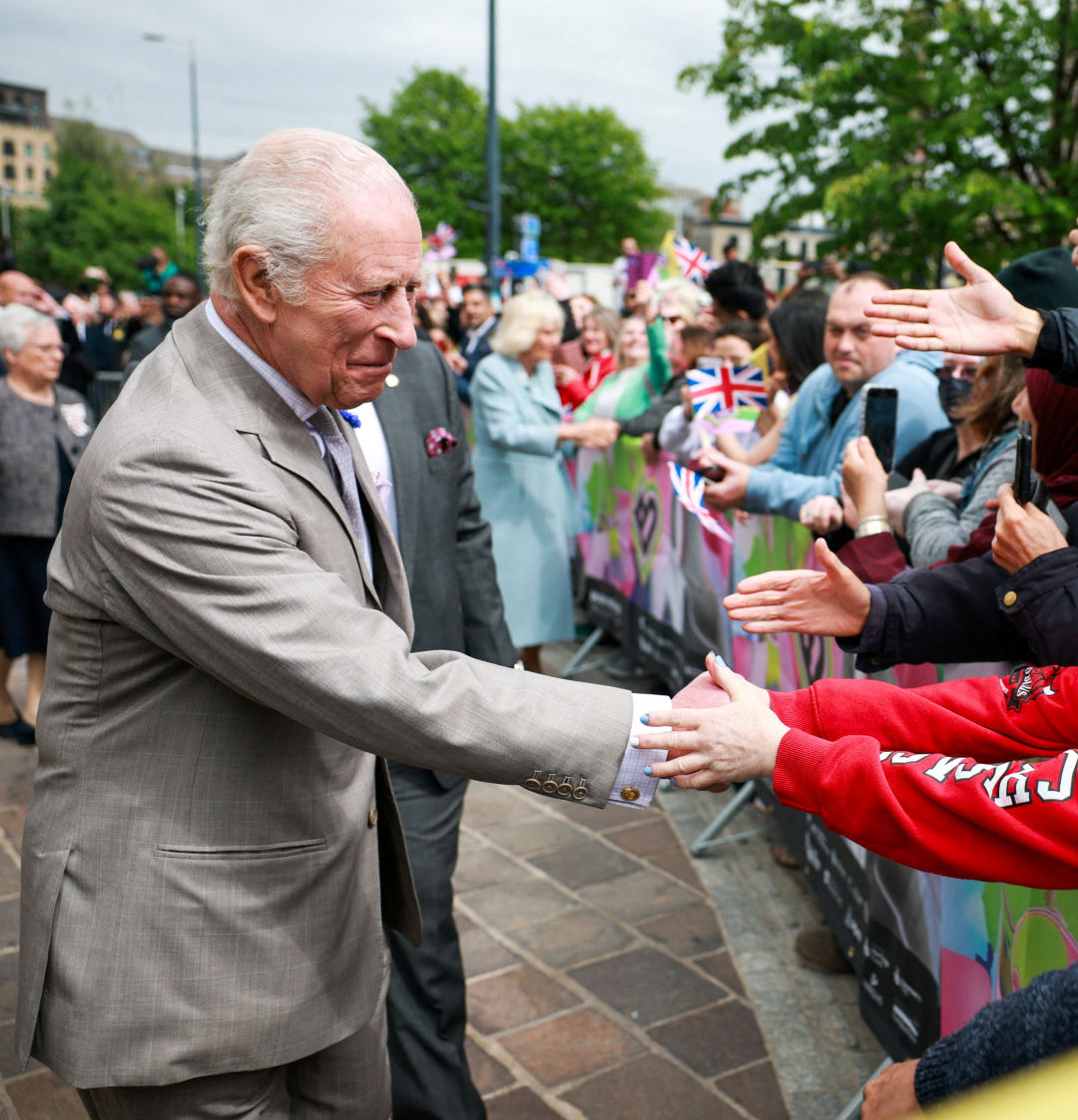 King Charles shaking hands with a crowd wearing a gray suit