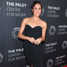 Meghan Markle wearing a strapless black dress on the red carpet and smiling
