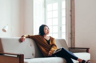 Young woman sitting on sofa and practising breathing exercises for anxiety