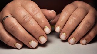person's hands with white nails with gold cuticle details