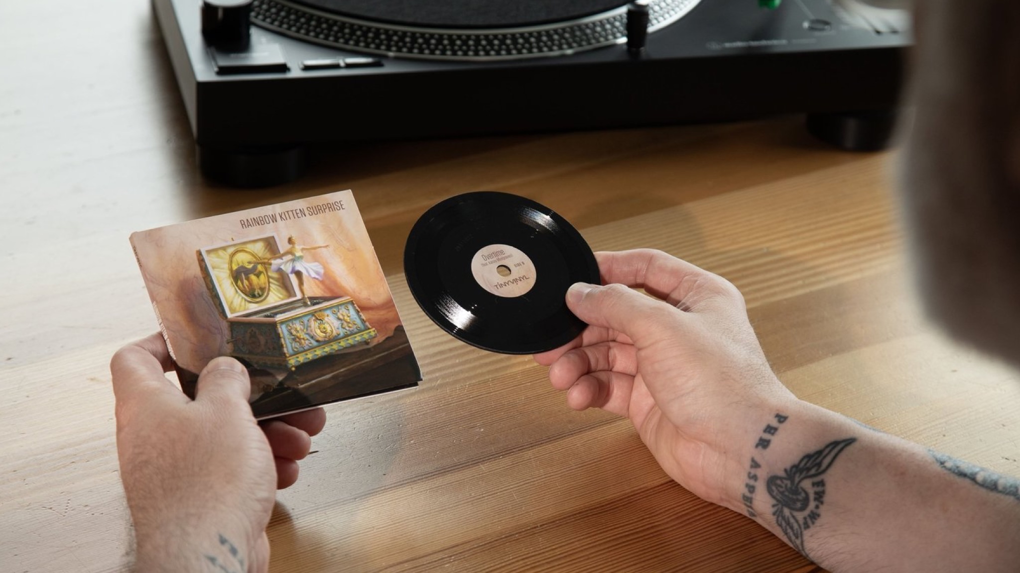 A Tiny Vinyl record being taken out of its sleeve in front of a black turntable on a wooden surface