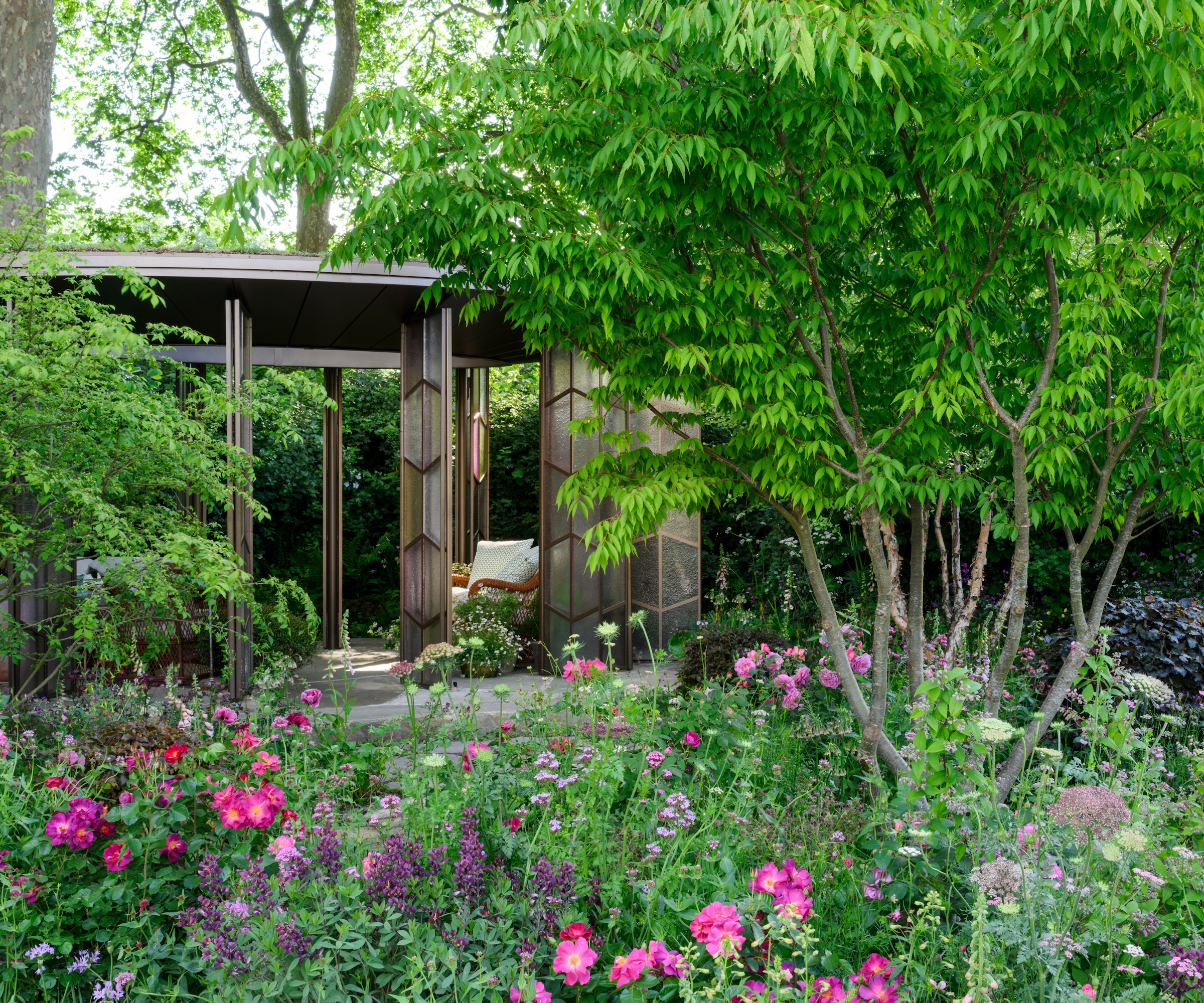 A modern glasshouse with pink, purple and lilac planting in the foreground