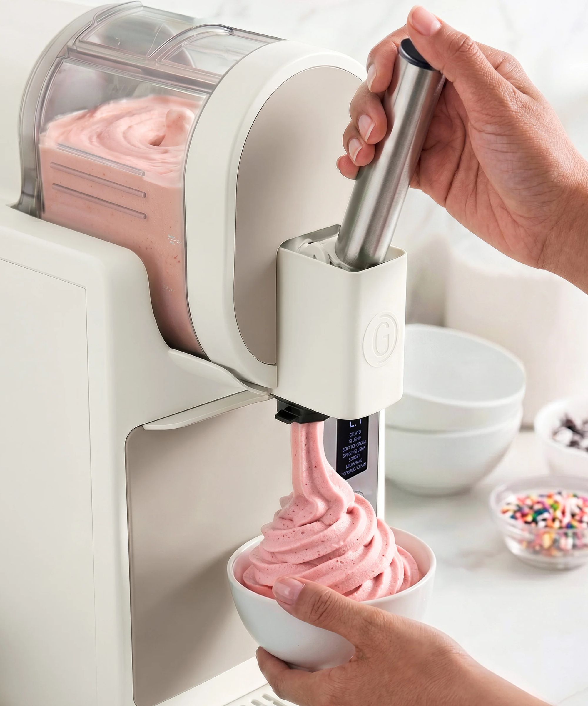 The GreenPan Frost Pro ice cream maker in white being used to make pink soft serve, being decanted into a white bowl