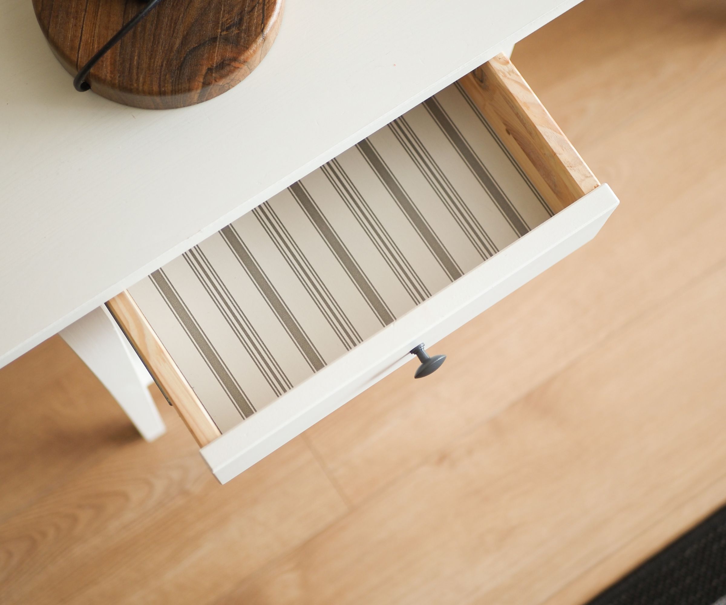 A white and grey striped drawer liner in an open bedside table drawer.