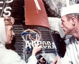 Mercury astronaut Scott Carpenter looks on as artist Cece Bibby puts the finishing touches on his capsule's Aurora 7 logo.