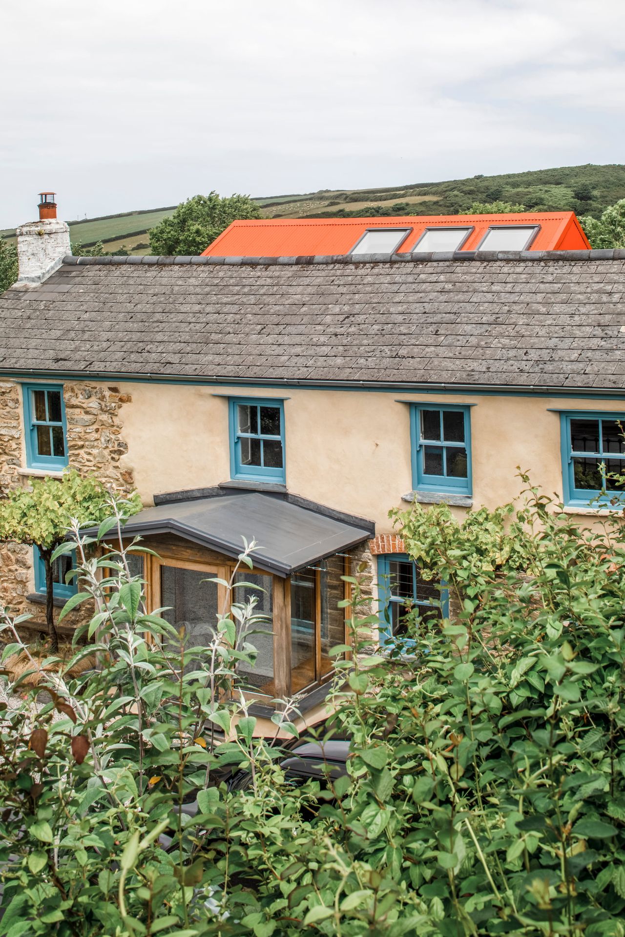 Cottage with blue painted windows and a porch with an orange modern extension to the rear