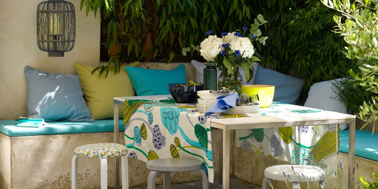 Alfresco dining area in garden with stone seating, yellow and blue cushions and table with stools