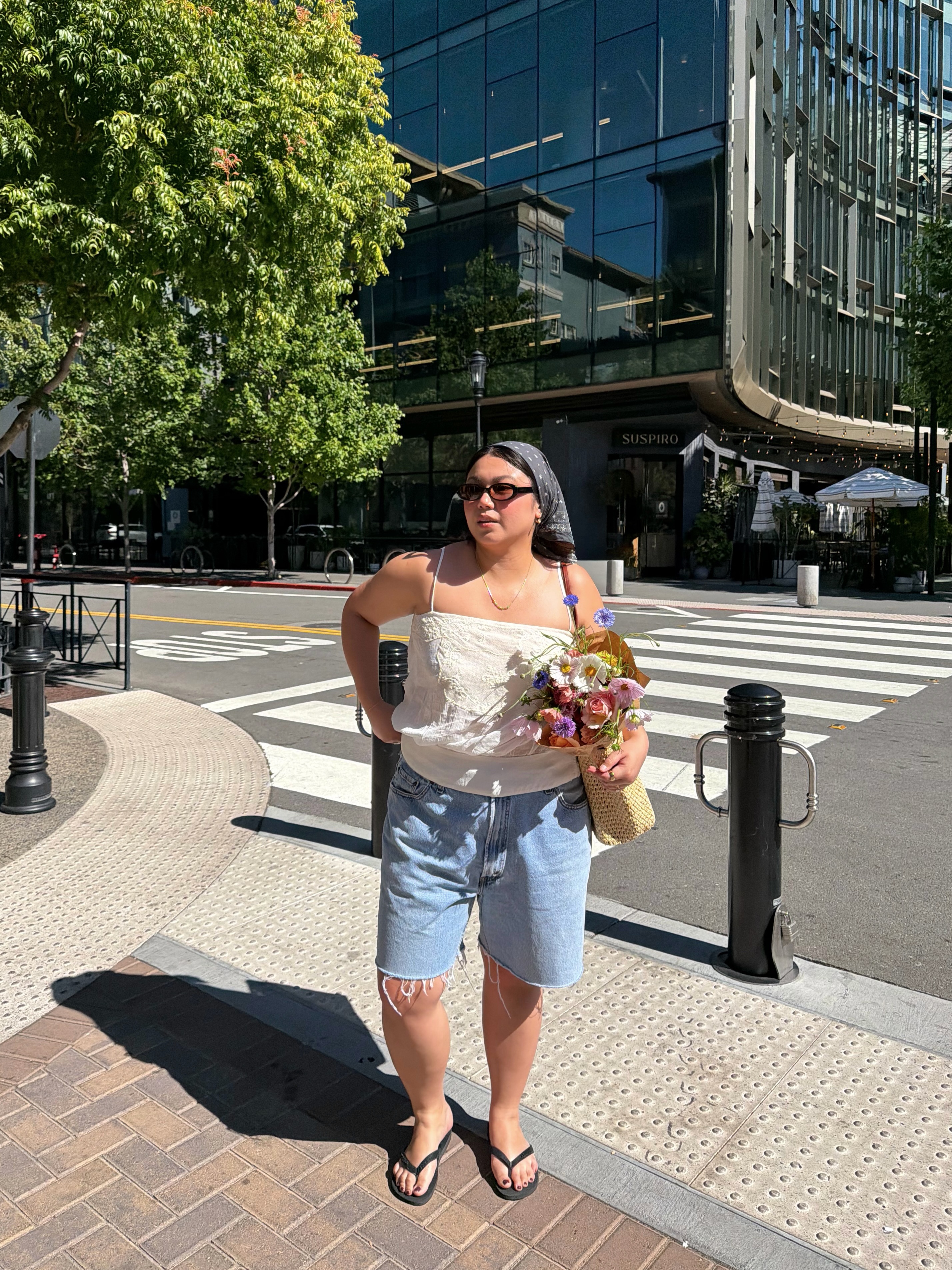 An image of @marina_torres wearing long denim shorts with flip-flops, a white camisole with a bandana.