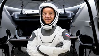 konstantin borisov in a spacesuit, crossing his arms in front of an open spacecraft hatch