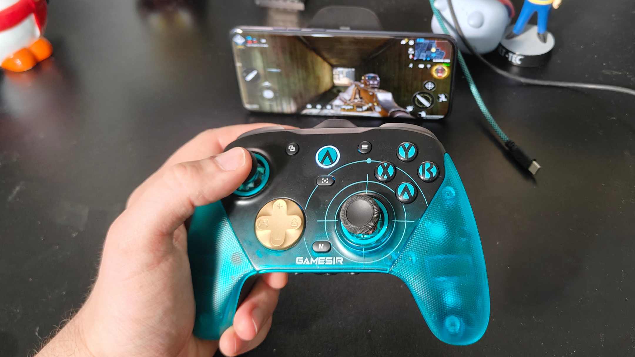 The GameSir G7 Pro 8k in a man's hand, with a phone showing Call of Duty Mobile in the background.