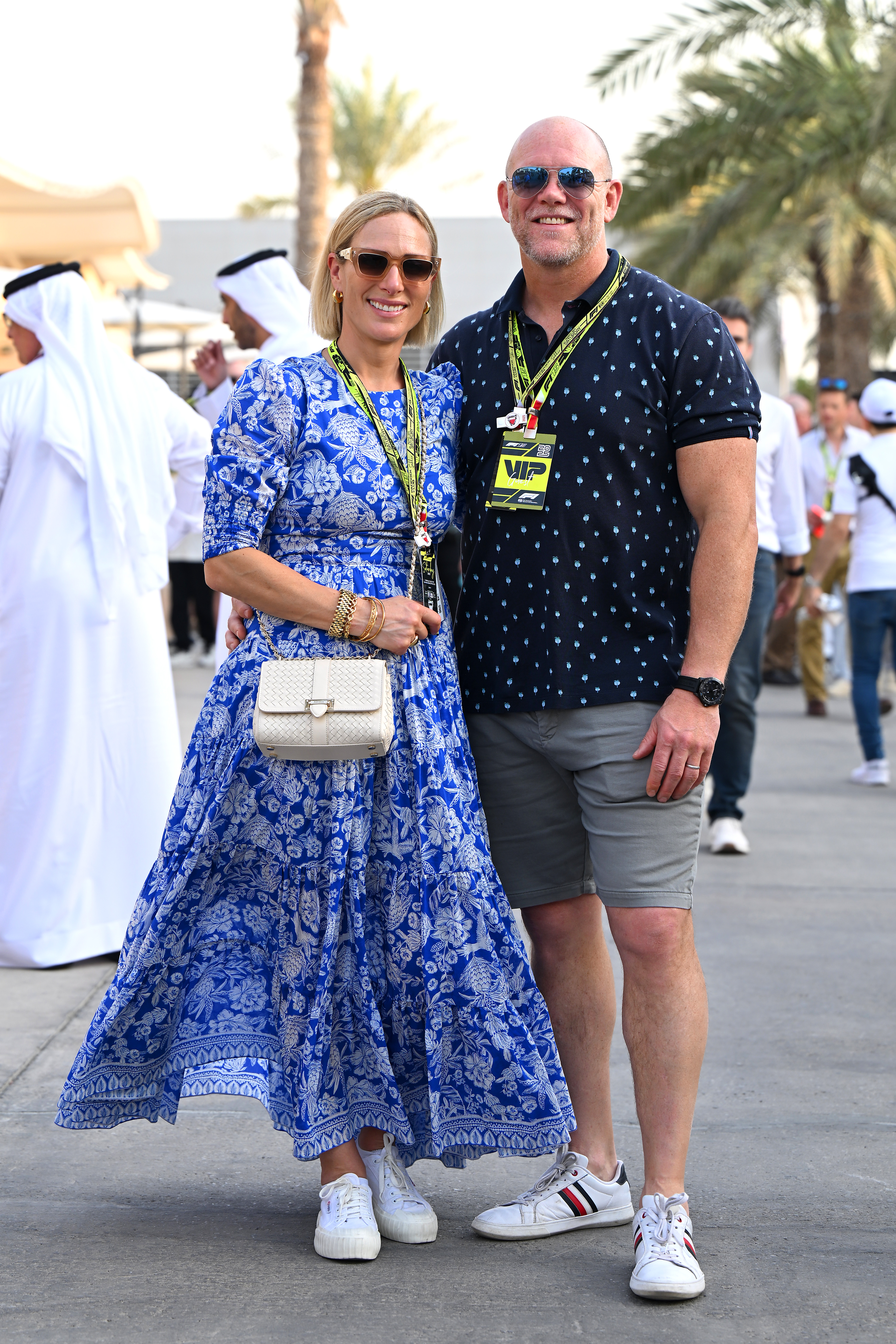 Zara Tindall wearing a blue floral dress and sneakers standing next to Mike Tindall, in shorts and a polo