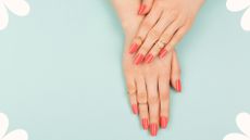 Bird's-eye view of woman's hands with long manicured nails painted coral to illustrate acrylic nails