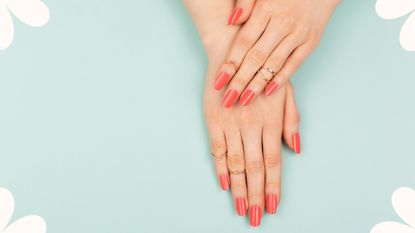 Bird's-eye view of woman's hands with long manicured nails painted coral to illustrate acrylic nails