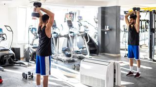 Man performing dumbbell overhead triceps extension in mirror