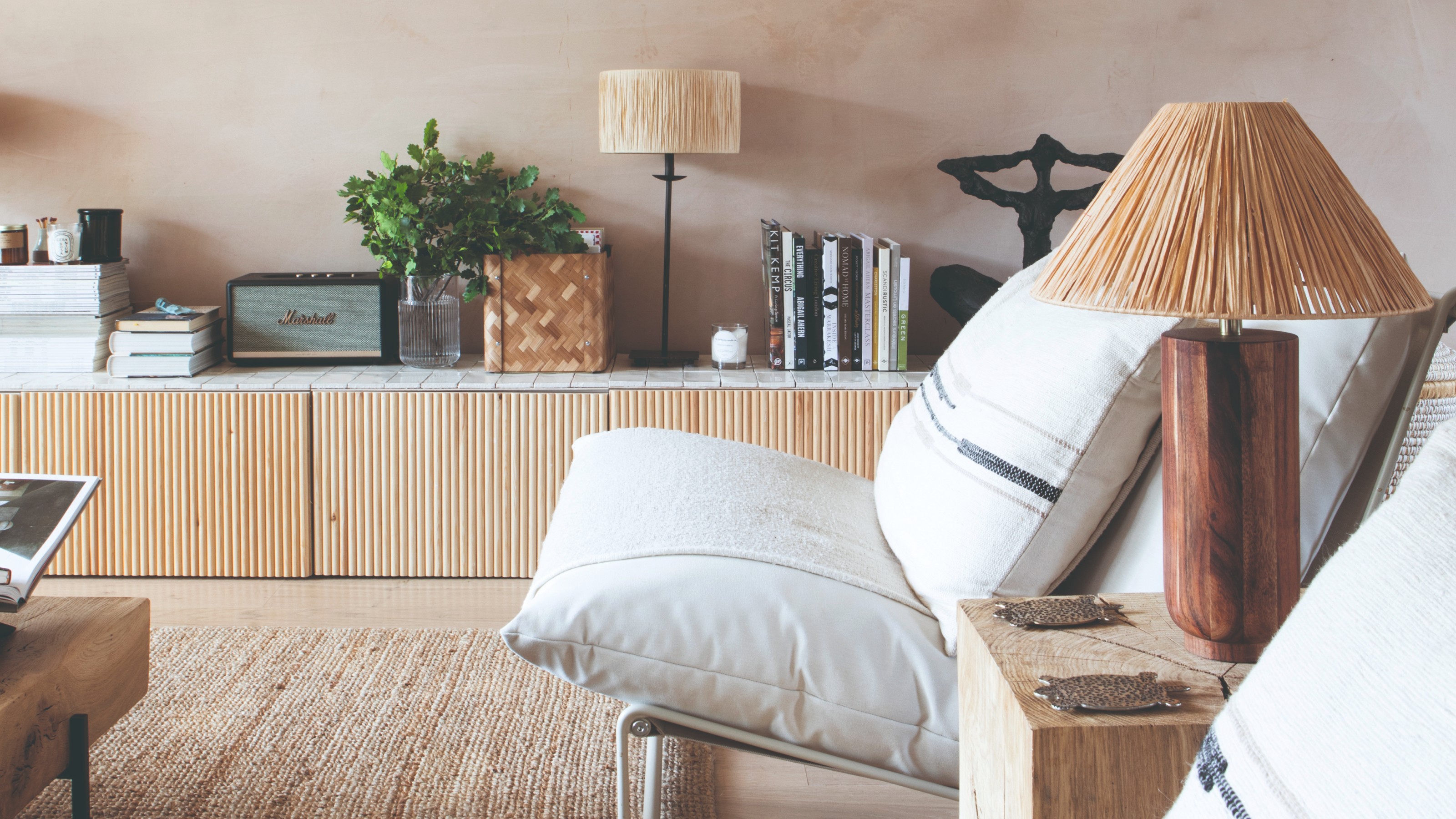 A living room painted in limewash with white lounge chairs, a reeded low sideboard and two raffia lamps