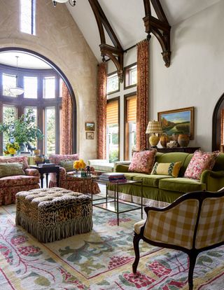 living room with green couch, floral armchairs, check armchair, leopard print pouffe, coffee table, colourful rug, vaulted ceiling, artwork, drapes blinds
