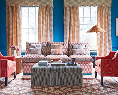 Large window curtain ideas with beige patterned curtains with a valance, in a blue living room with red armchairs and sofa