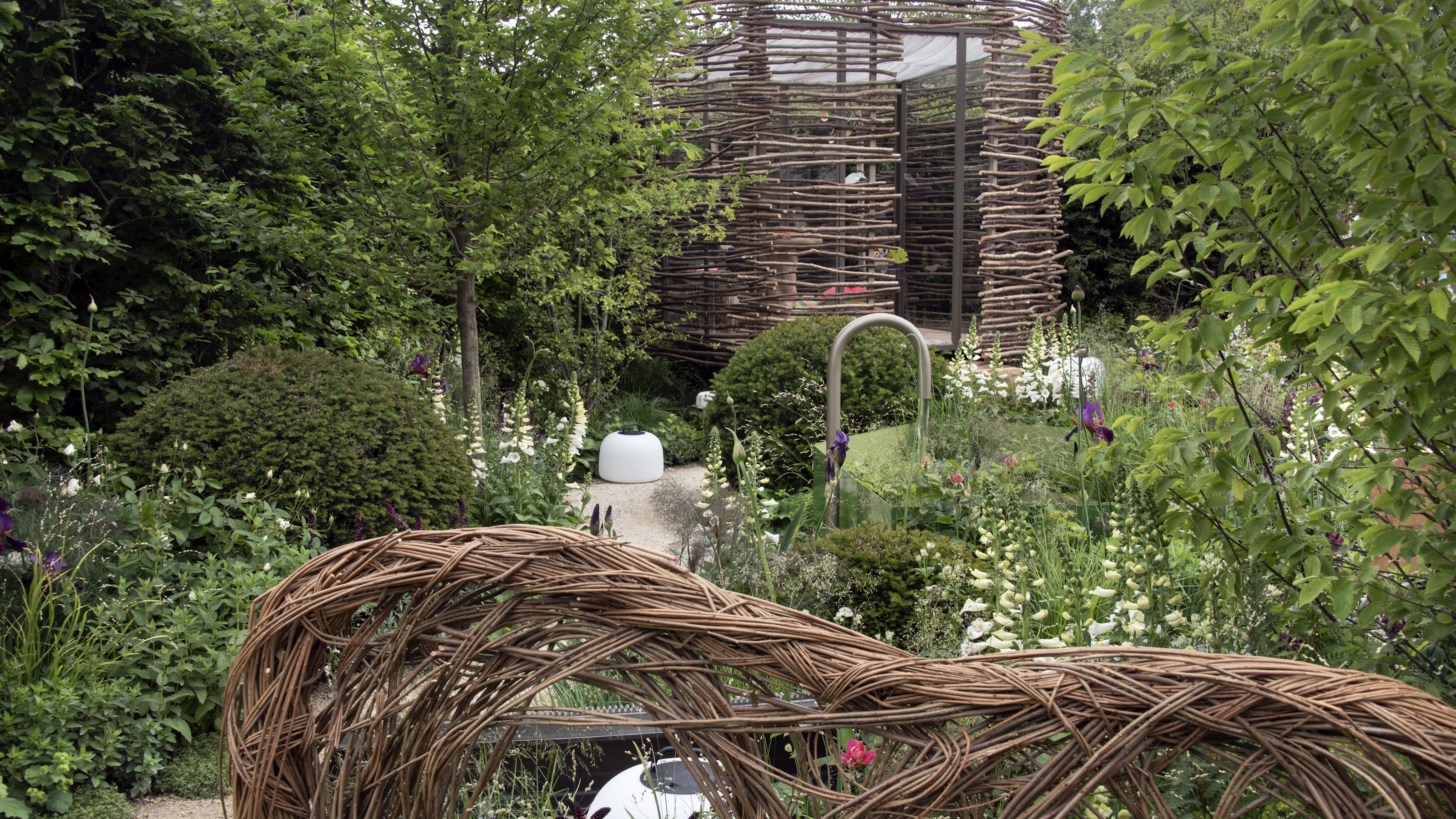 A summer garden with wicker features, trees, and white flowers at the RHS Chelsea Flower Show 2026