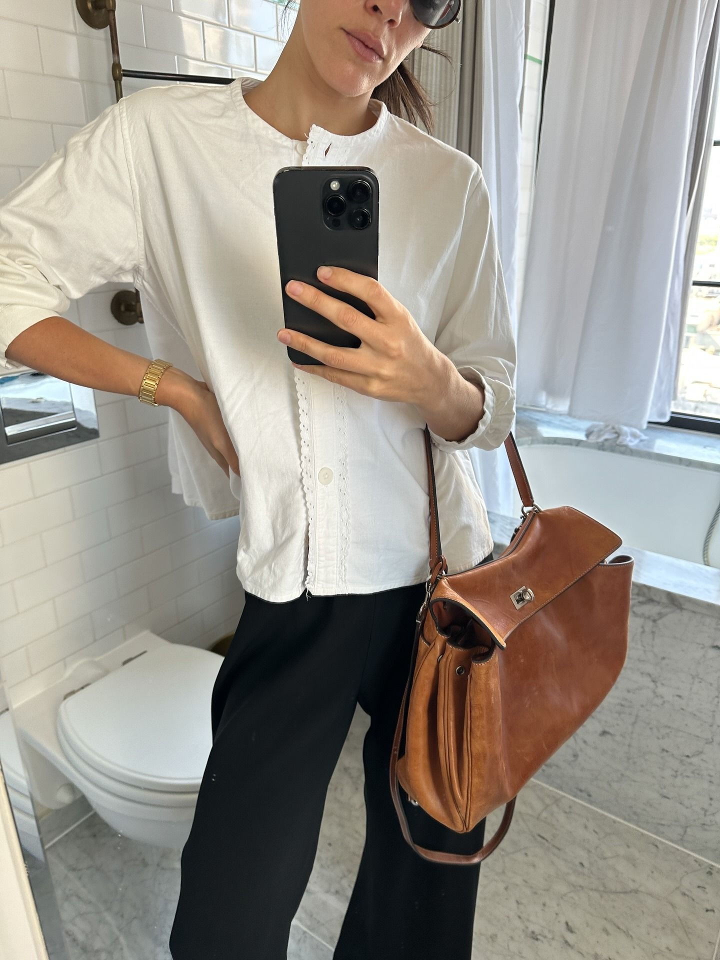 Ilana wears a white top, black trousers, and a distressed leather bag.