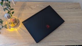 MSI GF63 Thin gaming laptop open on a wooden desk, with a plant next to it.