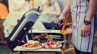 Man grilling sausages and vegetables outside in front of guests