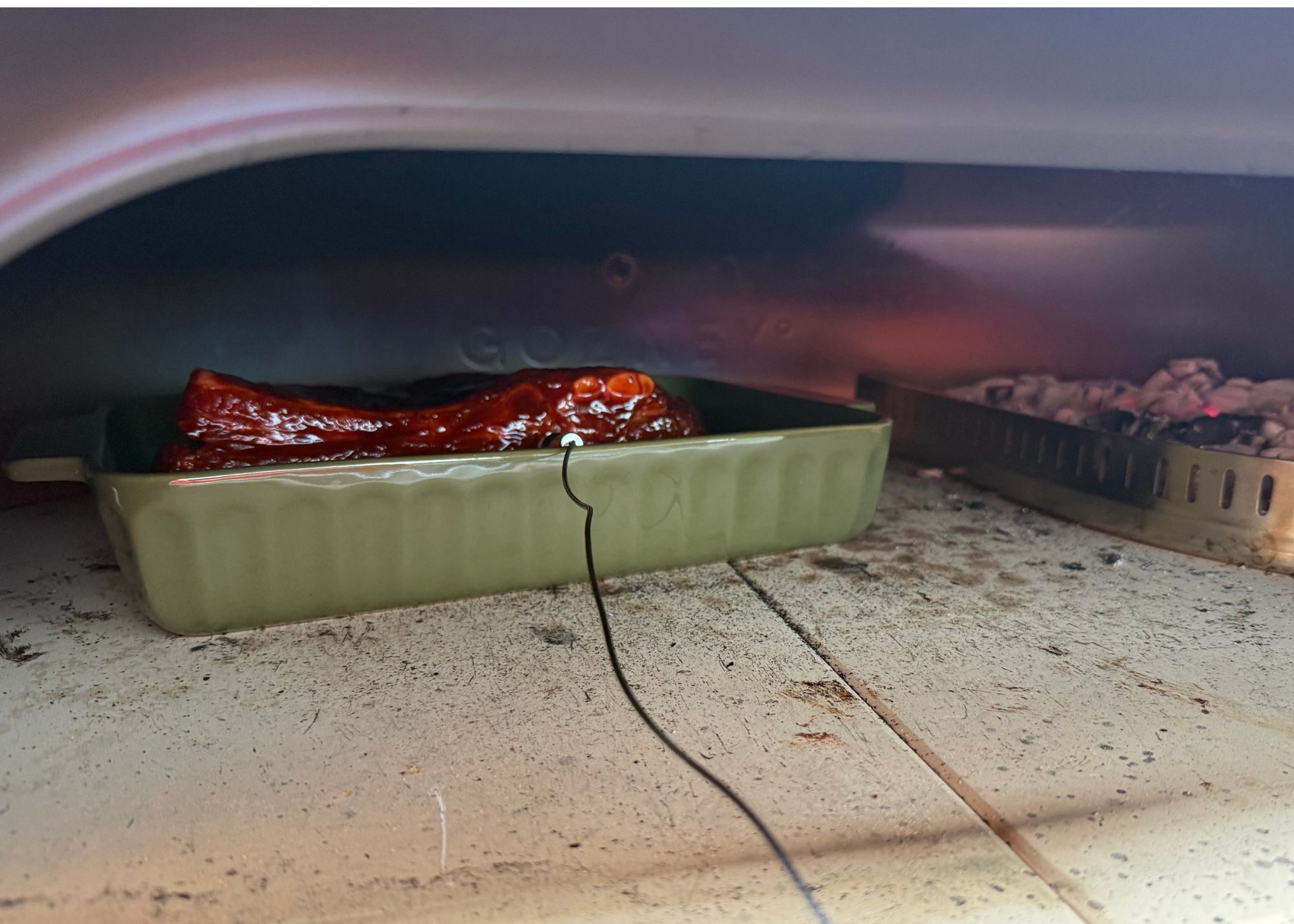 A close up of the inside of Gozney's Gome XL Gen 2 using the wood-fired section to cook a dish if ribs with the meat probe