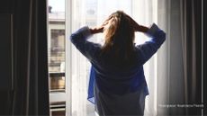 Woman running hands through her hair to represent anhedonia, looking out of window in apartment building