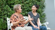 A mom and daughter sit together outside on a bench.