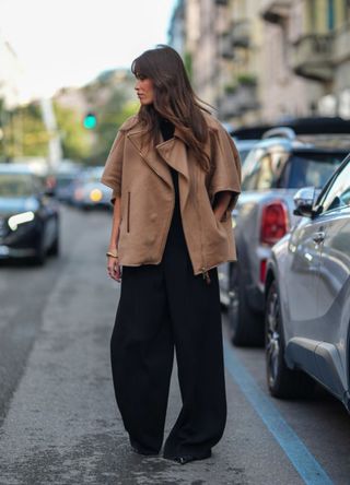 Alison Toby wears a light brown sleeve oversized unzipped jacket, black pants suit, and gold bracelet, outside Max Mara, during the Milan Fashion Week Spring/Summer 2024-2025 on September 19, 2024, in Milan, Italy