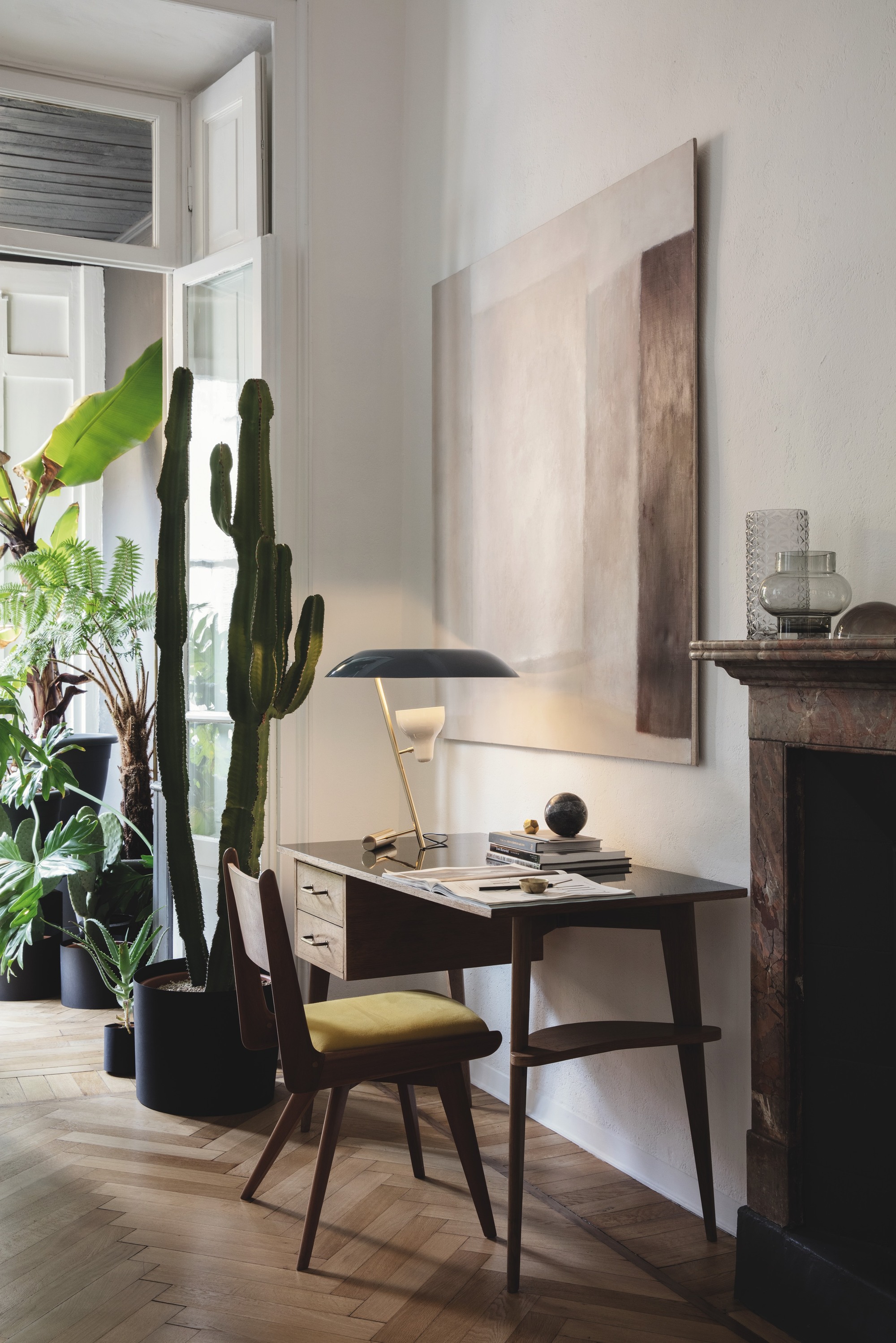 corner of mid-century style home with freestanding desk, chair and table lamp, a potted cactus in the corner and large artwork on the wall