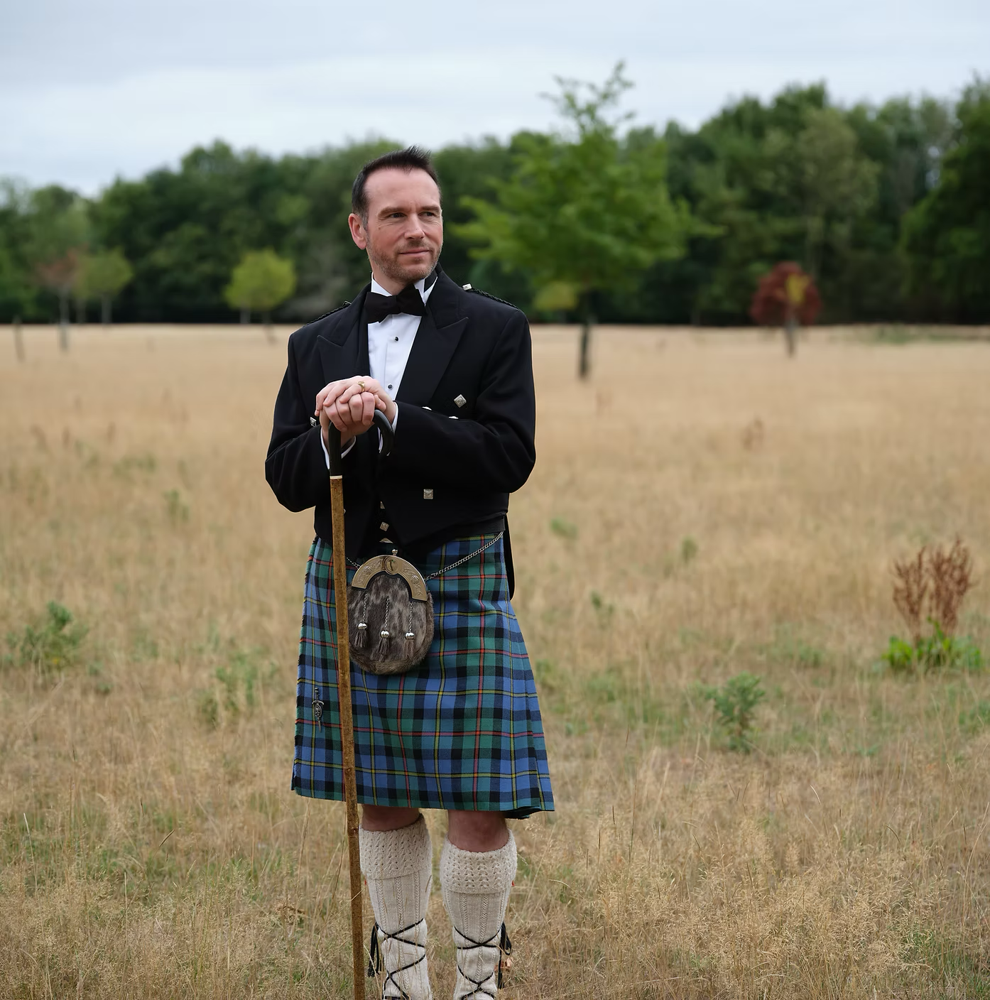 Grant Harrold wearing a kilt standing in a field holding a walking stick