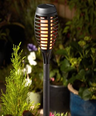 A Tiki torch style solar light surrounded by plant pots