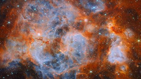 A nebula made of clouds of gas and dust with stars forming within. In the centre and out to the left it is filled with thin, wispy blue gas that forms delicate layers. 