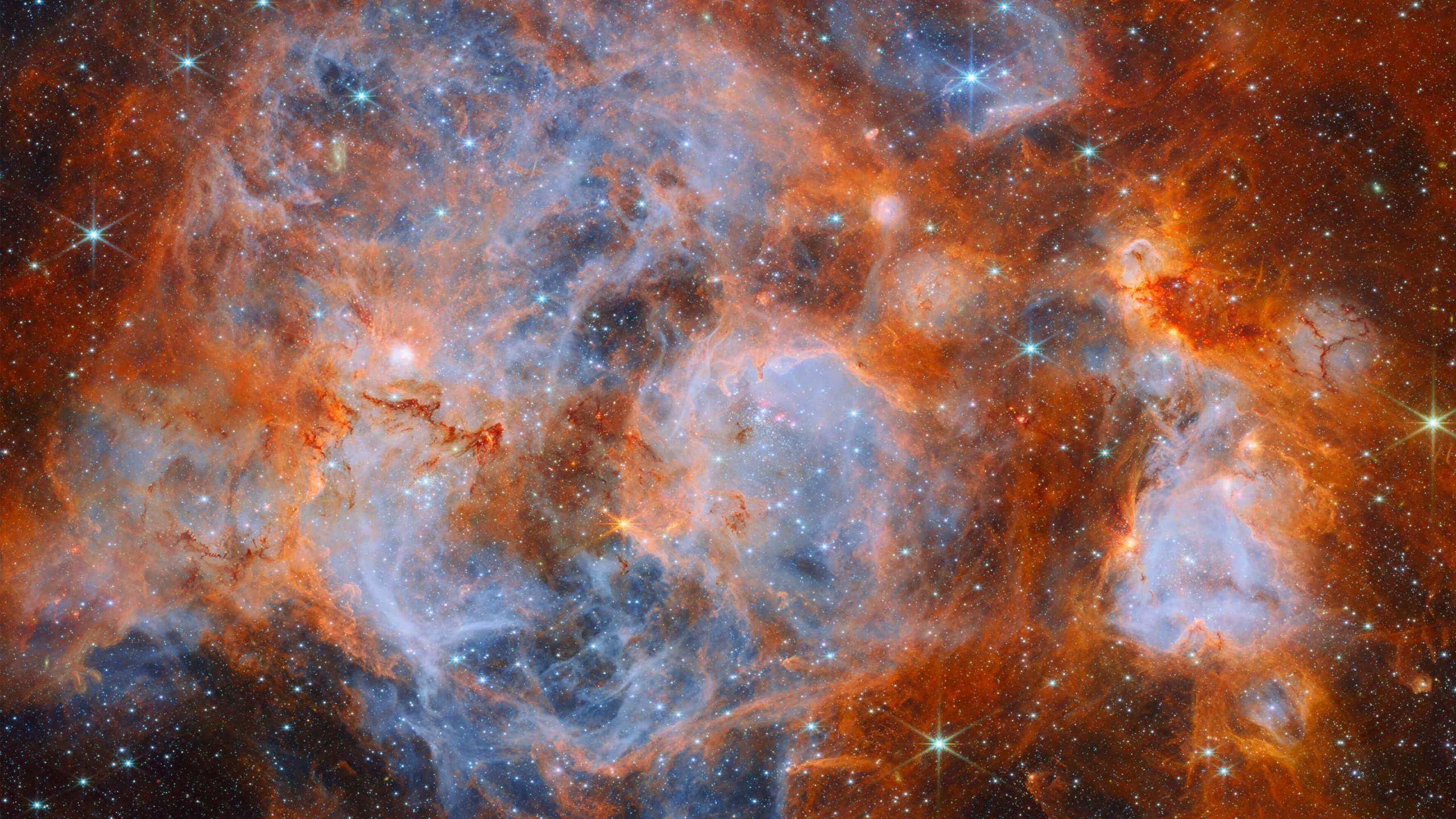 A nebula made of clouds of gas and dust with stars forming within. In the centre and out to the left it is filled with thin, wispy blue gas that forms delicate layers. 
