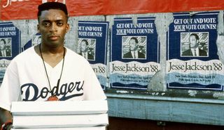 Spike Lee stands with pizzas in front of a brick wall in Do The Right Thing.